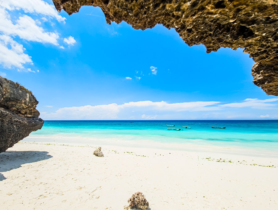 Vit sandstrand och turkost hav under en klippa på Zanzibar en solig dag i mars