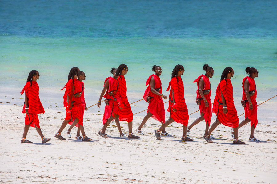 Masajer i röda kläder promenerar längs en vit strand på Zanzibar